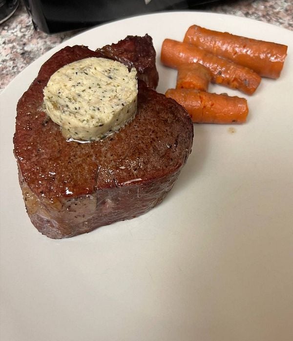 A beautifully cooked filet mignon topped with herb butter and accompanied by glazed carrots.