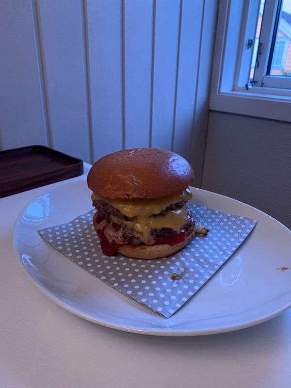 A delicious double Angus cheeseburger with cheddar cheese and ketchup is presented on a plate.