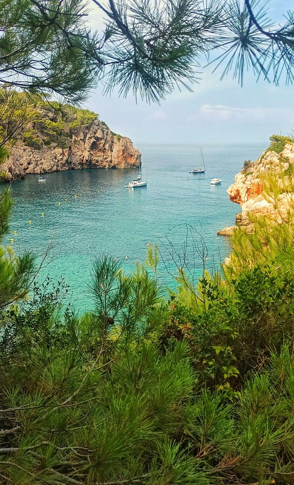 A serene coastal view featuring boats anchored in clear turquoise waters surrounded by rocky cliffs and lush greenery.
