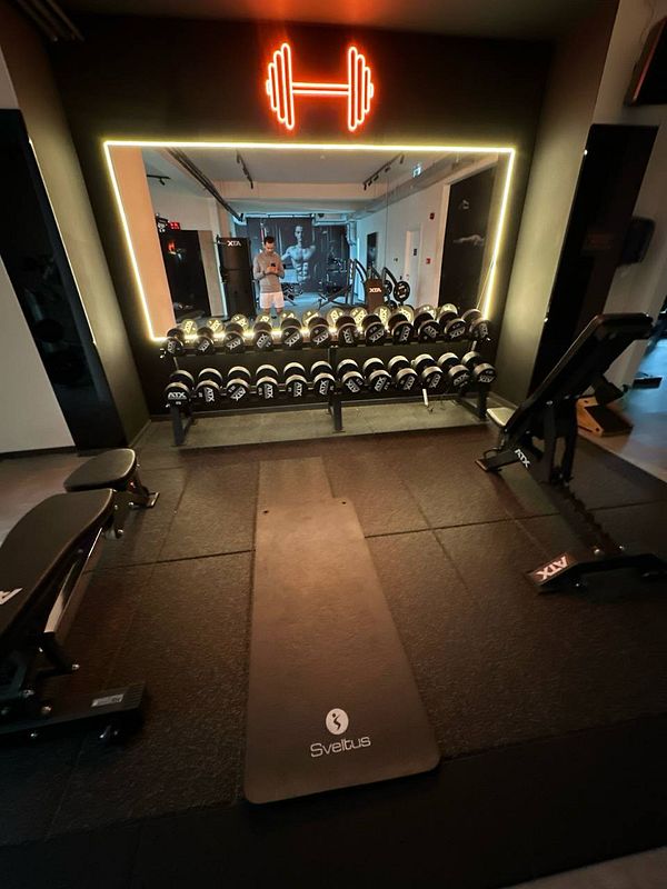 A modern gym interior featuring weights, exercise equipment, and a neon sign.