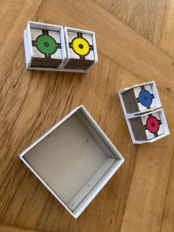 The image features several small boxes containing colored game pieces on a wooden surface.