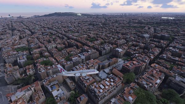 Aerial view of Barcelona with a Qatar Airways airplane flying over the city.