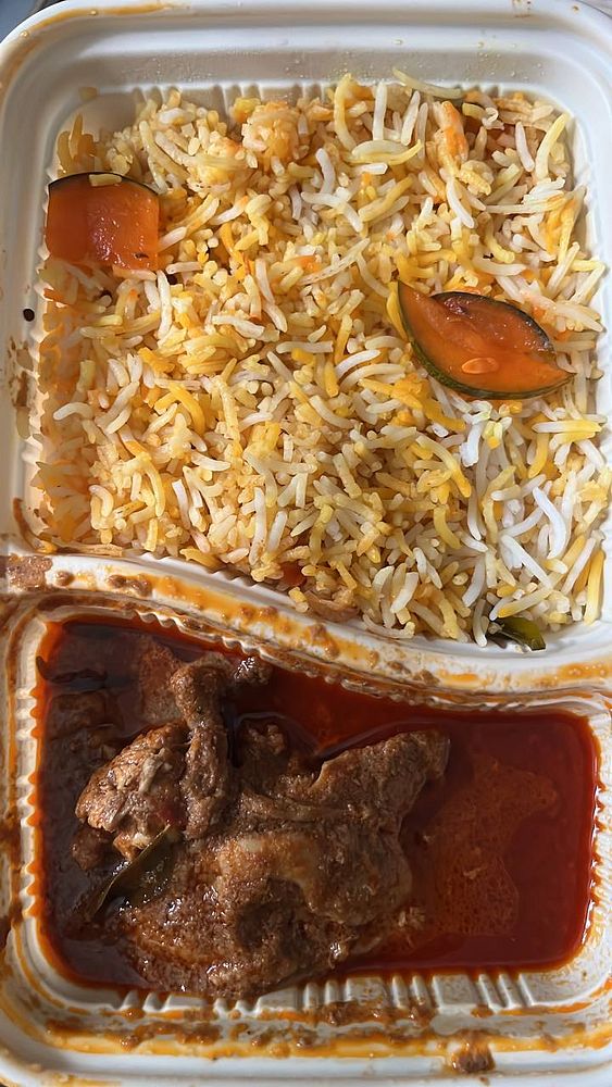 A takeout container filled with biryani rice and curry chicken.