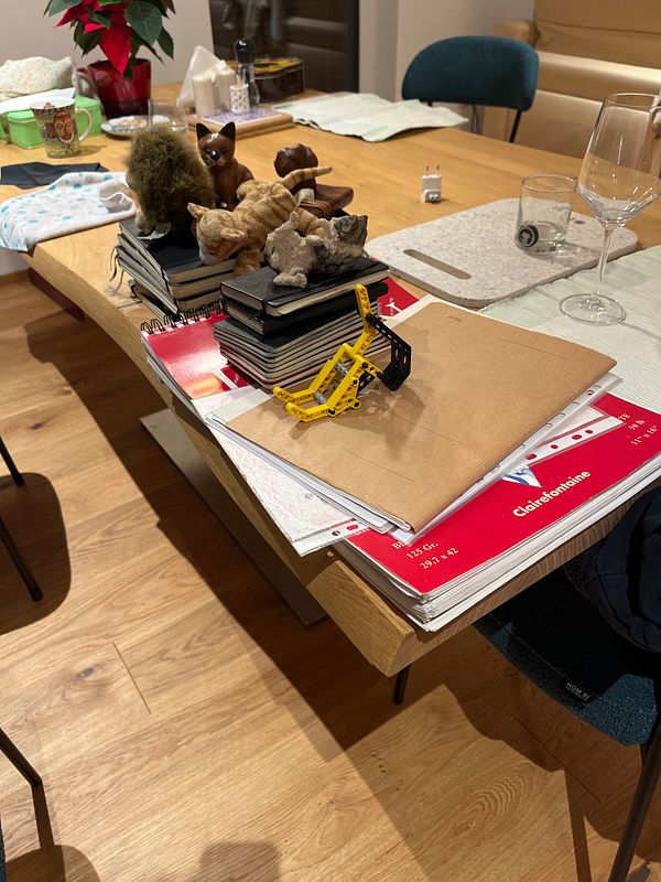 A cluttered dining table filled with various items, including notebooks, small figurines, and a calendar.