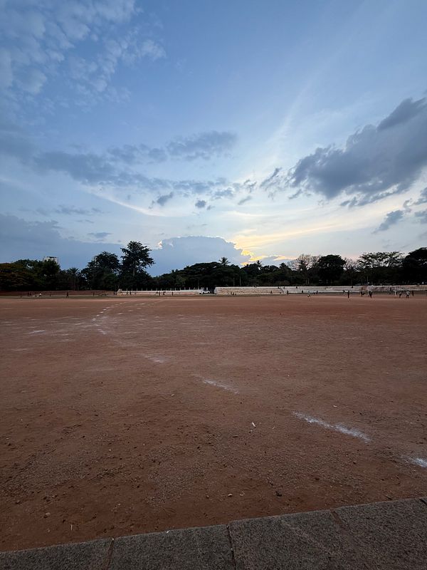 A serene outdoor scene featuring a large, empty dirt field under a colorful sky at dusk.