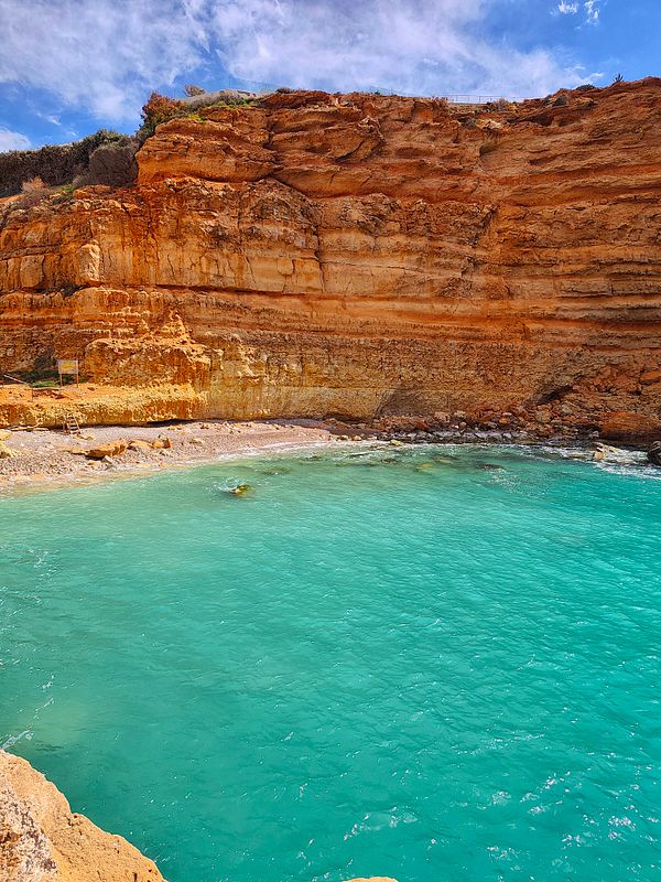 A scenic mountain hiking trail surrounded by dense, lush green forest under a partly cloudy sky.