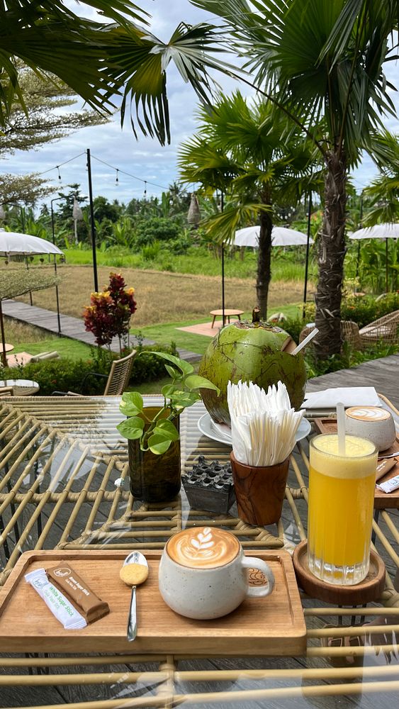 A serene outdoor breakfast setting featuring coffee, fresh juice, and tropical greenery.
