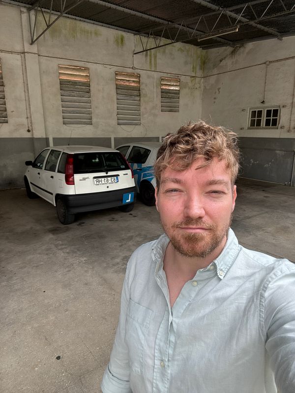 A person stands in a parking area with two cars in the background, preparing for a driving class.