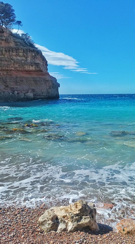 A cozy indoor setting with a steaming cup of coffee on a saucer placed on a wooden table beside a partially visible red candle holder and a smartphone.