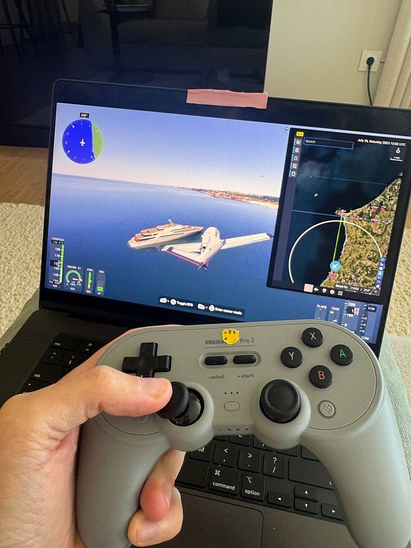 A person is holding a gaming controller while playing a flight simulation game on a laptop.