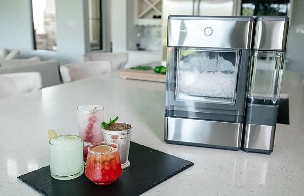A stylish ice maker is displayed alongside colorful cocktails on a modern kitchen countertop.