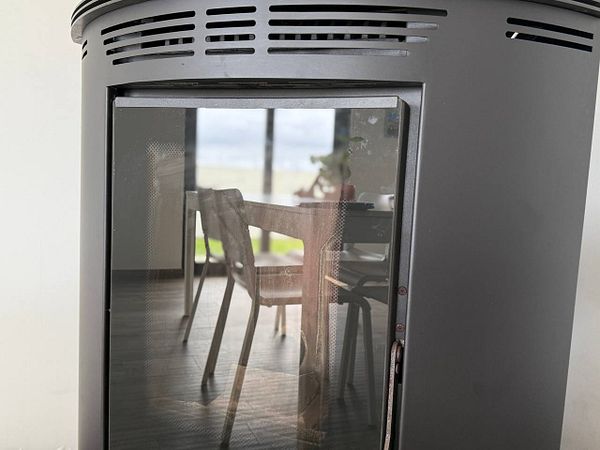 A close-up view of a pellet stove with a reflection of a dining area in its glass front.
