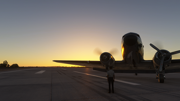 A pilot stands on the runway in front of a vintage aircraft during sunset.