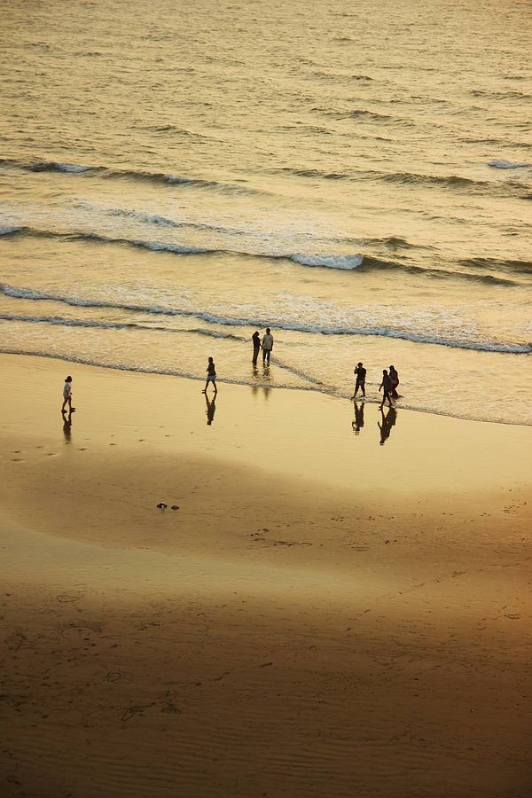 A serene beach scene at sunset with people walking along the shore.