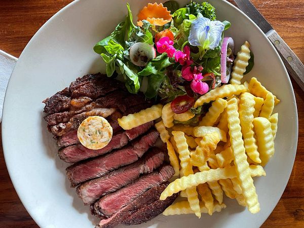A plate featuring a 100-day grain-fed ribeye steak, a fresh salad, and crinkle-cut fries.