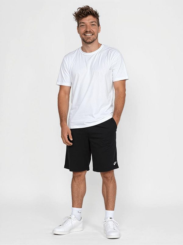 A smiling man stands confidently in casual athletic wear against a plain background.