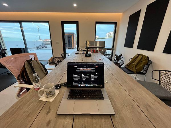 A modern coworking space featuring a large wooden table with a laptop and various personal items.