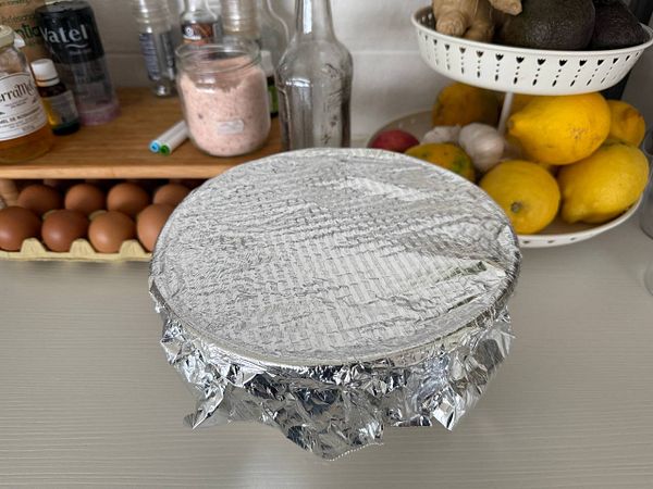 A covered bowl of marinating chicken sits on a kitchen counter surrounded by various ingredients.