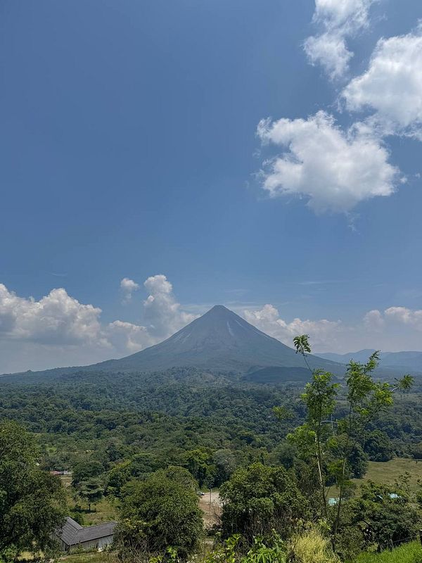 A majestic volcano rises above a lush green landscape under a clear blue sky.