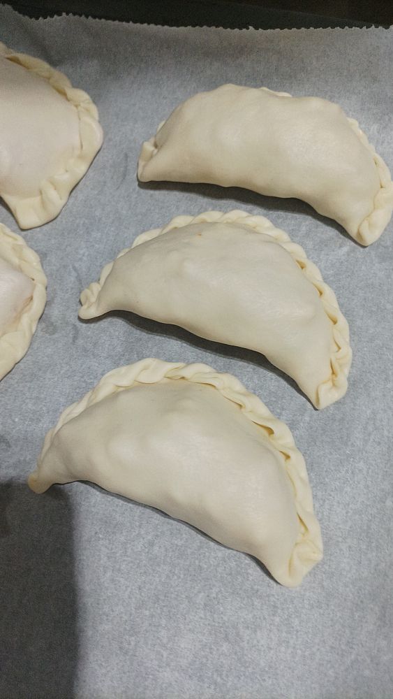 The image features several uncooked chicken empanadas arranged on a baking sheet.