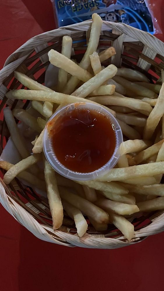 A basket filled with French fries and a small cup of dipping sauce.