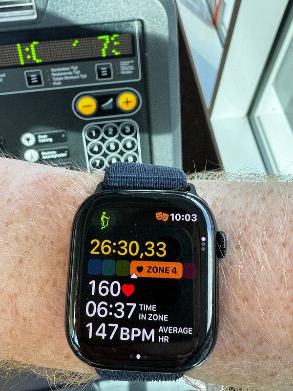 Photo of a gym interior featuring two stairmaster machines and a weightlifting area with barbells and benches.