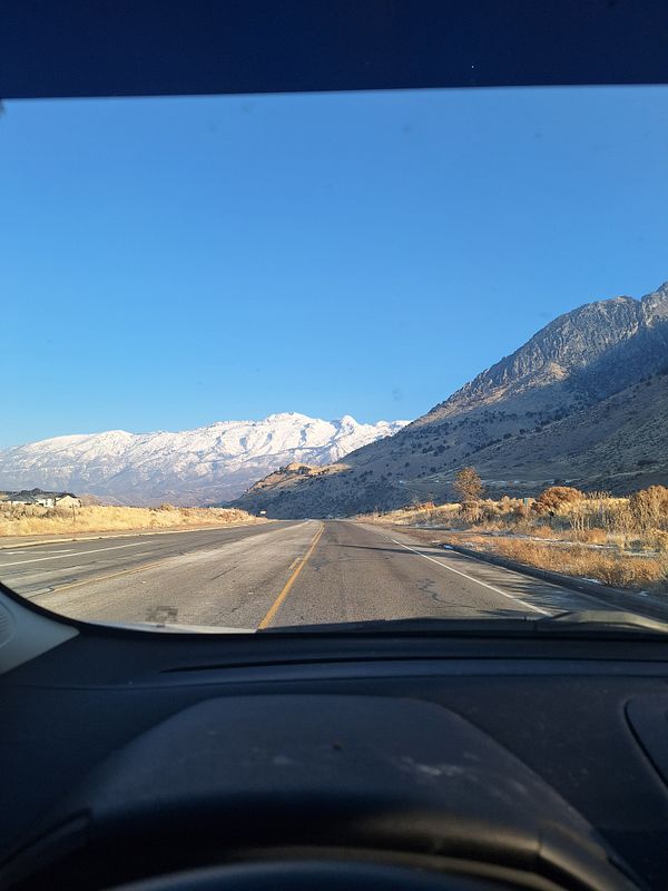 A scenic view of a road leading towards snow-capped mountains under a clear blue sky.