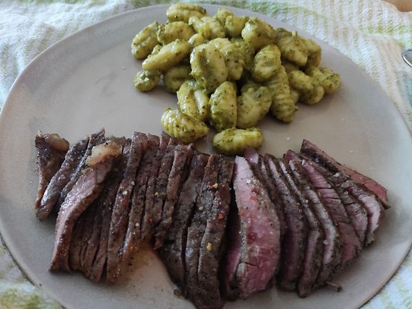 A plate featuring sliced steak and pesto gnocchi.