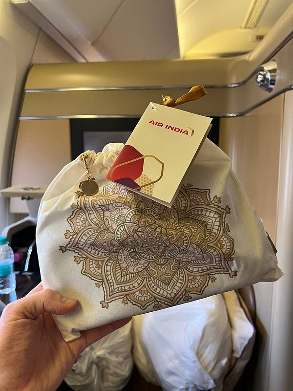 A hand holds a decorative pouch with an Air India tag in an airplane cabin.