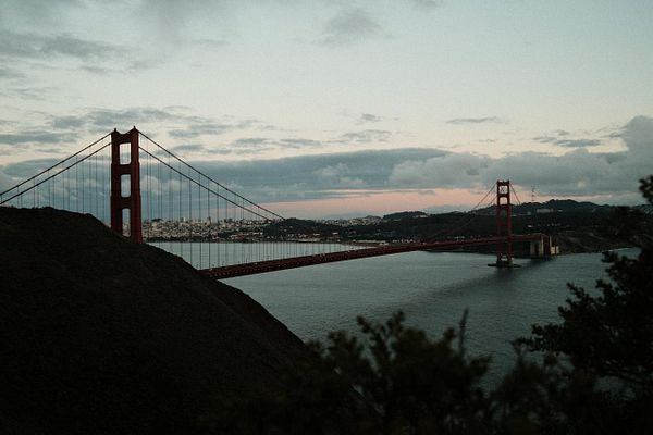A scenic coastal cityscape of San Francisco featuring the Golden Gate Bridge and nearby hills under a partly cloudy sky.