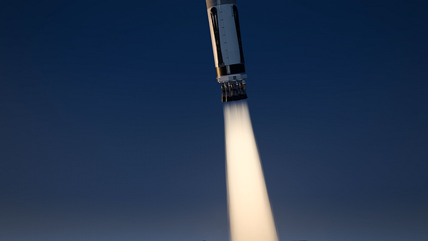 A detailed 3D rendering of a rocket engine firing with visible exhaust plume against a clear dark blue sky.