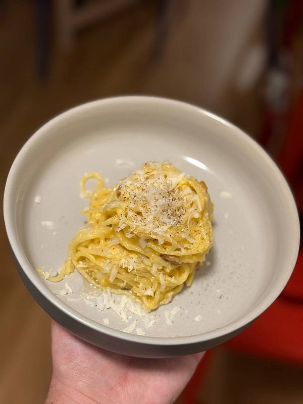 A plate of spaghetti carbonara is being held in a hand.