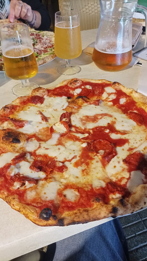 A delicious pizza Napolitana is served alongside drinks in a casual dining setting.