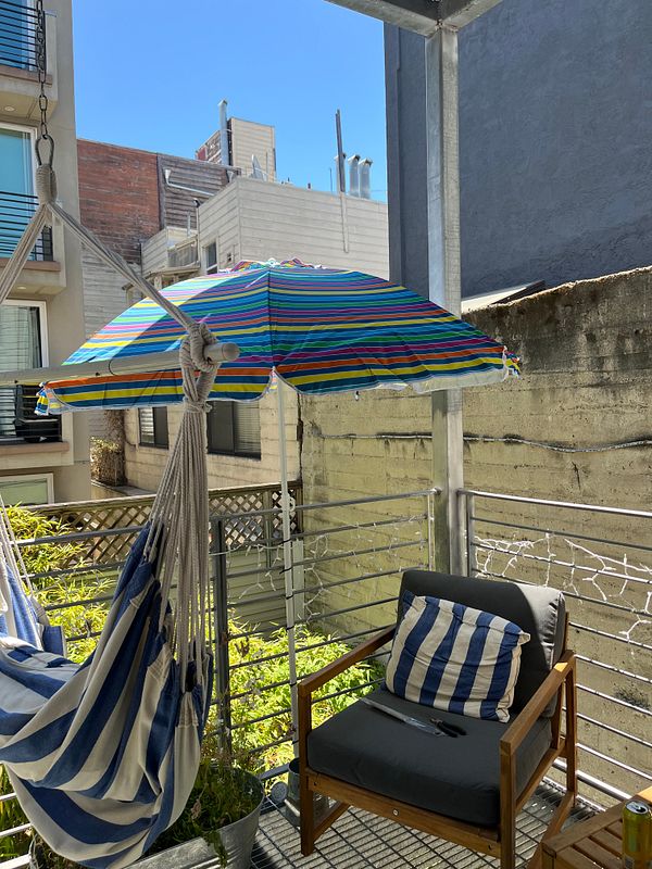 A colorful parasol is set up on a balcony with a hammock and a chair.