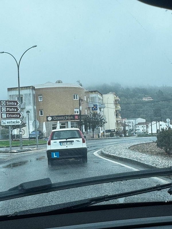 A learner driver is navigating a roundabout in a foggy, rainy environment.