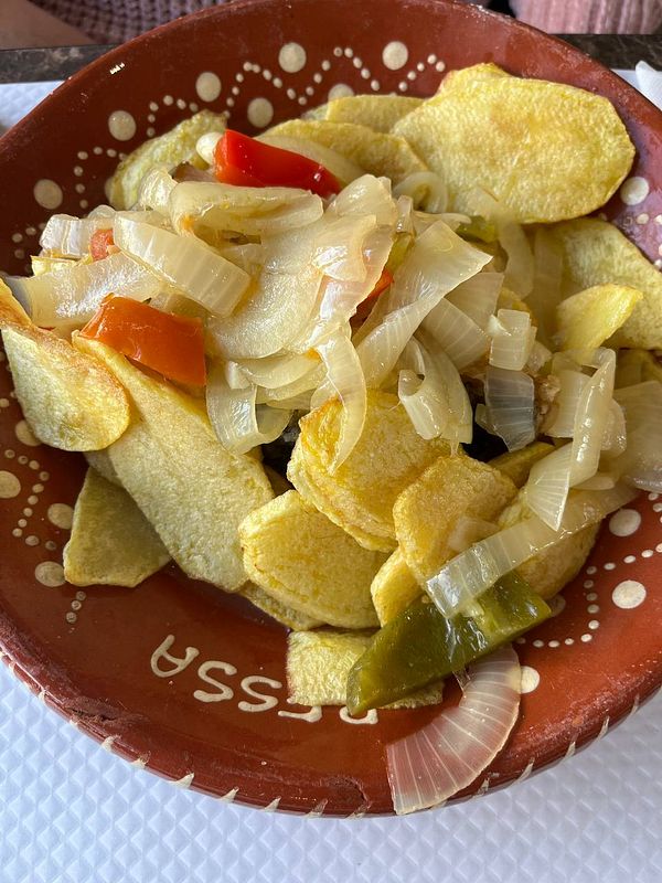 A traditional Portuguese dish featuring fried potatoes topped with sautéed onions and colorful bell peppers.