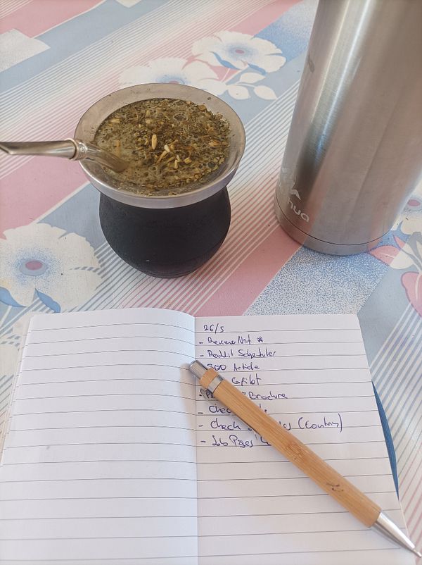 A cozy workspace featuring a traditional mate drink, a notebook with tasks, and a thermos.