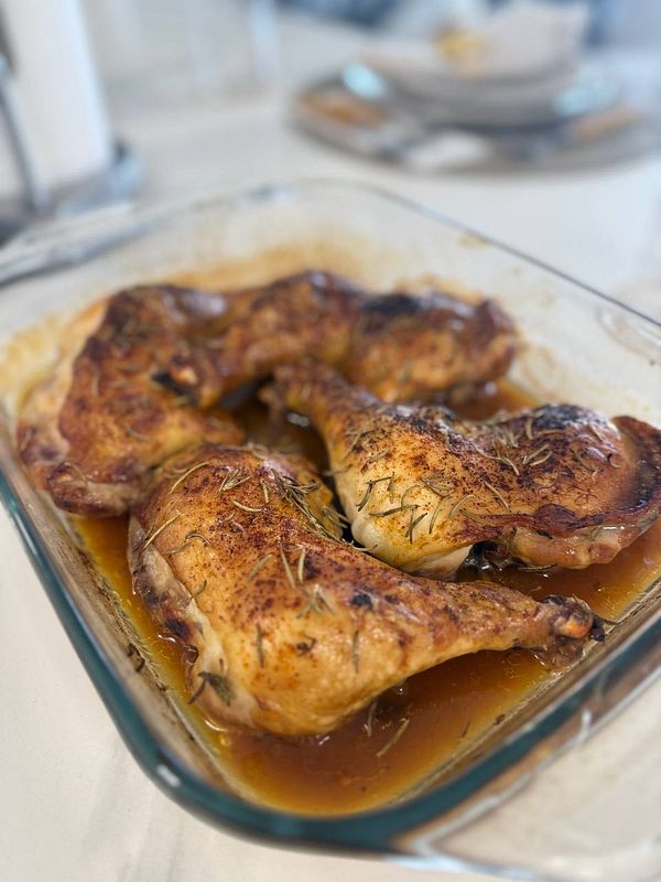 A glass dish contains marinated chicken pieces, showcasing a golden-brown color and garnished with herbs.