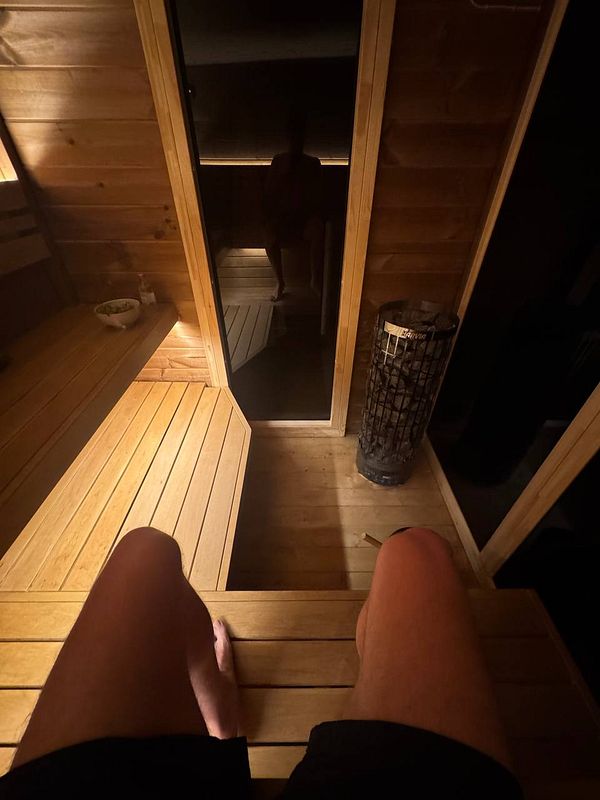 A person is sitting in a wooden sauna, with their legs visible and a dimly lit interior.