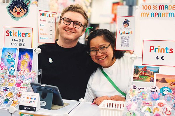 A cheerful couple is selling art merchandise at a market stall.