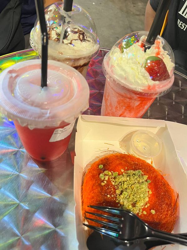 A colorful display of kunafa and drinks on a reflective table.