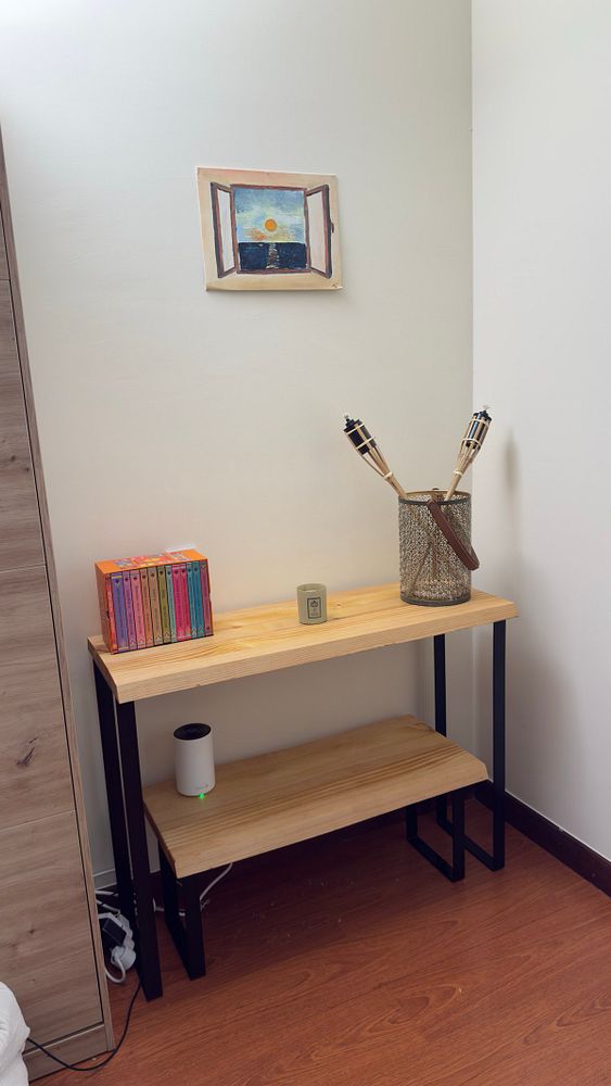 A corner of a room featuring a wooden shelf with decorative items and a painting on the wall.