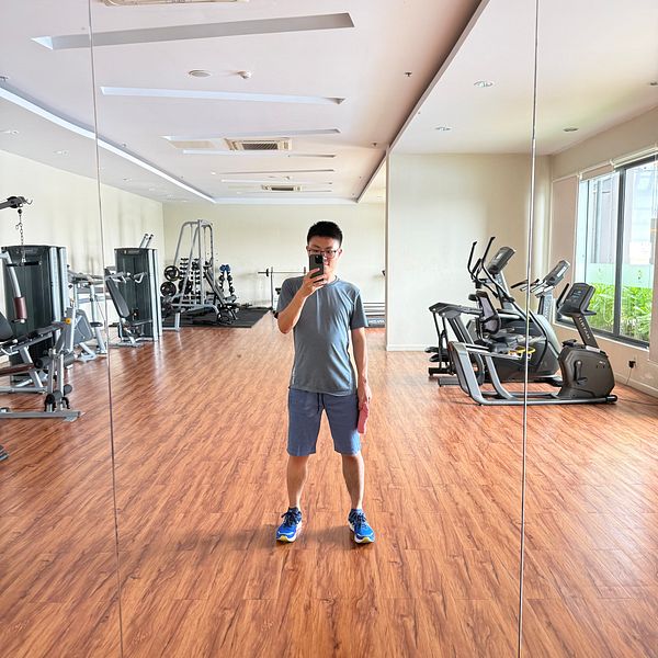 A person stands in an empty gym, taking a selfie in the mirror.