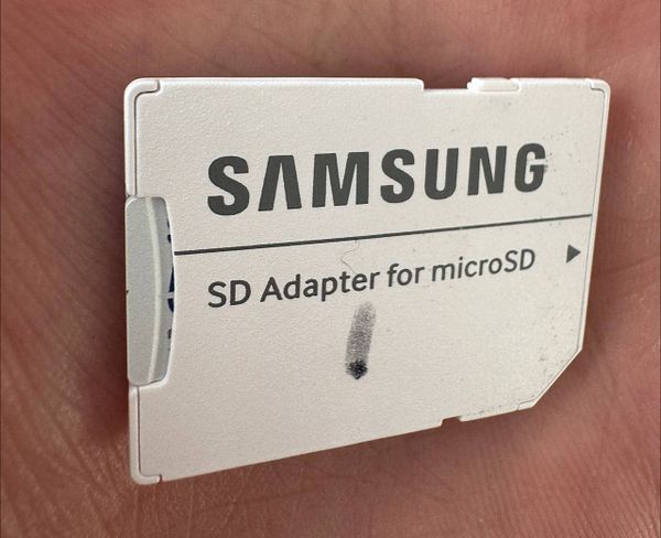 A Samsung SD adapter for microSD cards is held in a person's hand.