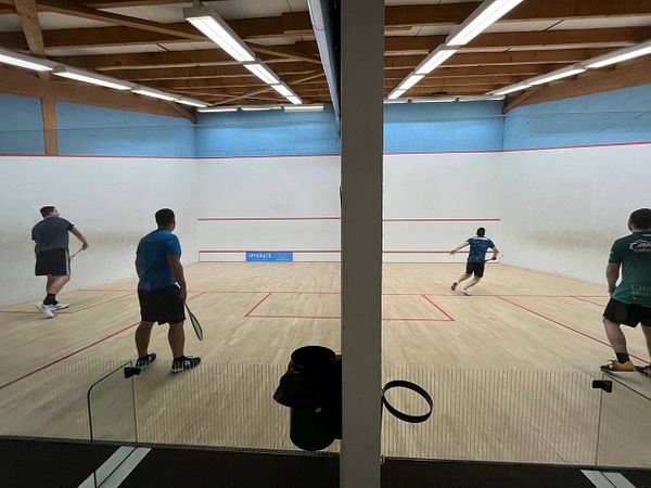 Four players are engaged in a game of squash in a well-lit court.