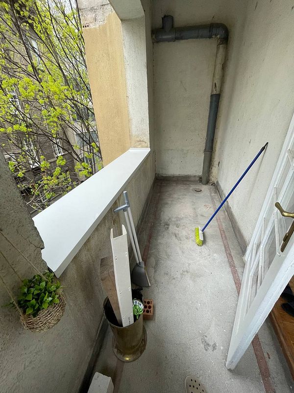 A balcony area is shown, featuring cleaning tools and a view of greenery outside.