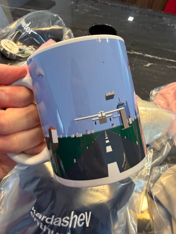 A hand holds a colorful mug featuring a graphic design of an airport runway and an airplane.