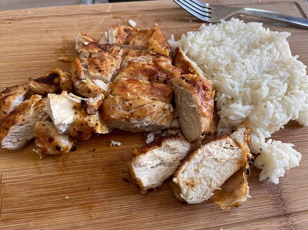 A plate of sliced grilled chicken served with a side of fluffy white rice.