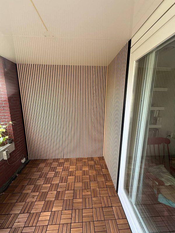 A modern loggia area featuring installed acoustic panels on the ceiling above a seating arrangement with a table and plants.