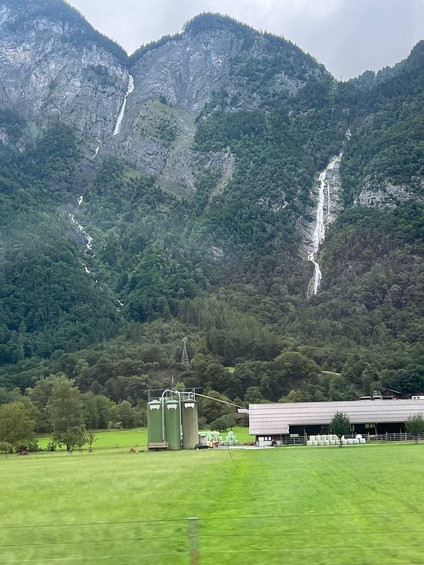 A scenic view of mountains with waterfalls and a farm in a lush green valley.